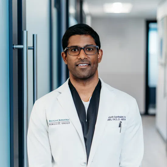 Smiling male doctor wearing glasses and white coat standing in a modern medical hallway