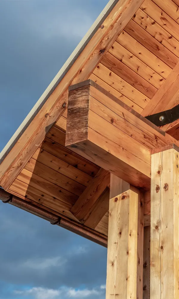 Close-up of wooden beams and roof structure with metal bolts under a cloudy sky.