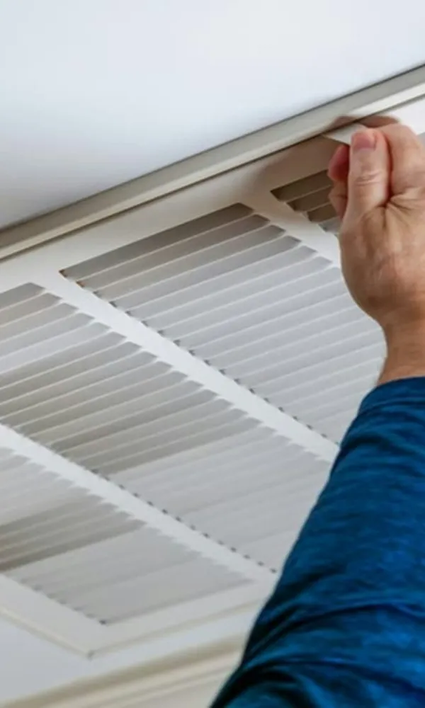 Person removing or installing a white ceiling air vent grille in a modern home ceiling.