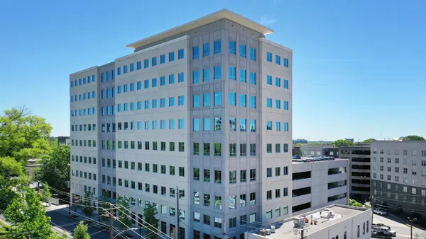 Modern multi-story office building with reflective windows under clear blue sky in an urban environment.