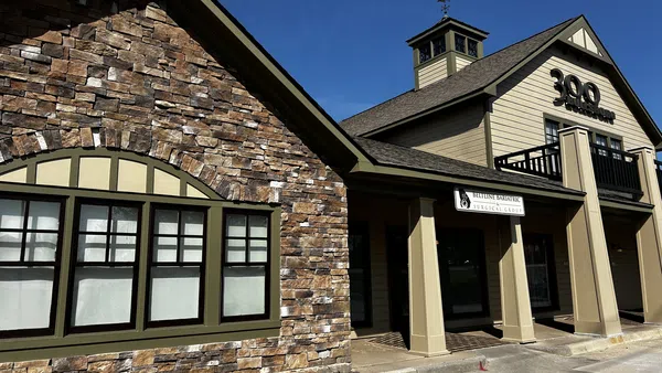 Modern two-story commercial building with stone facade and beige siding under clear blue sky