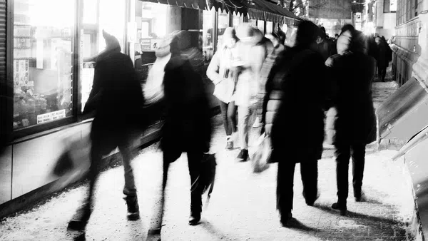 Black and white photo of people walking on a snowy city sidewalk at night with blurred motion effect.