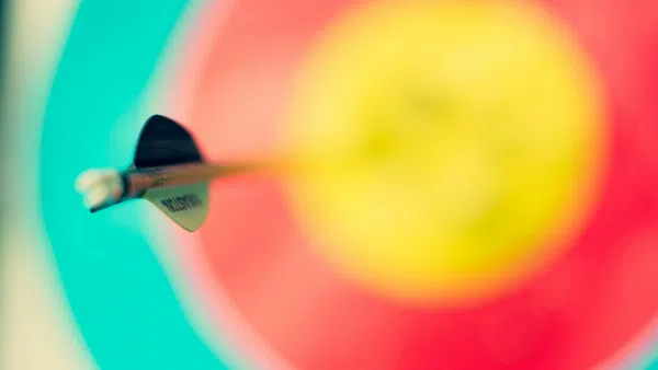Close-up of an arrow hitting the center of a colorful archery target with teal, red, and yellow rings.