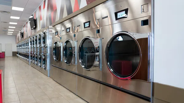 Modern laundromat with rows of stainless steel washing machines and dryers in a clean, bright interior.