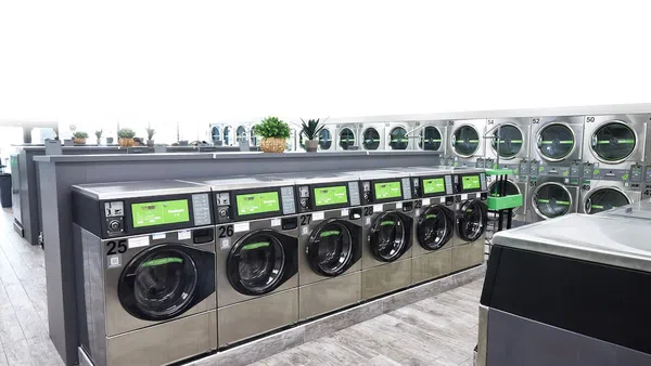 Modern laundromat with rows of stainless steel front-loading washing machines and dryers in a bright, clean space.