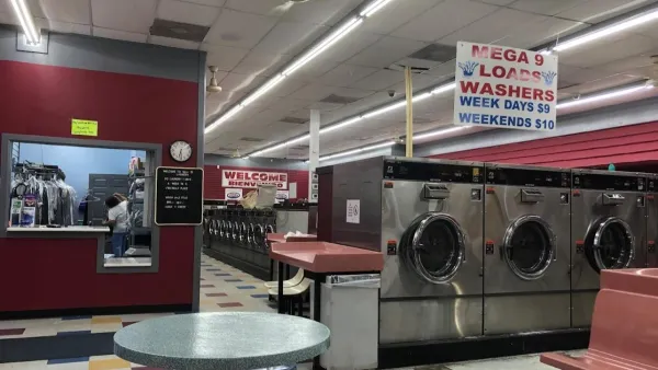Interior of a laundromat with rows of washers, folding tables, seating, and colorful tiled floor under fluorescent lights.