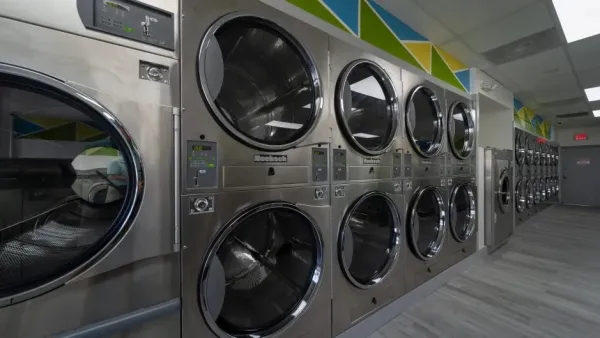 Row of stainless steel commercial dryers in a brightly lit modern laundromat interior.