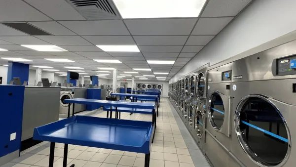 Interior of a spacious laundromat with rows of industrial washers and blue folding tables.