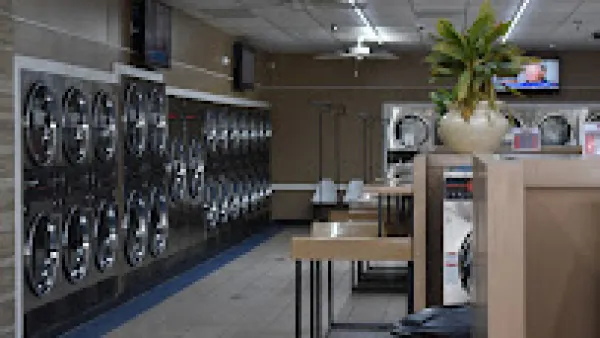Interior of a laundromat with rows of washing machines and folding tables under fluorescent lighting