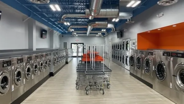 Spacious modern laundromat with rows of front-loading washers and dryers, carts, and bright lighting.