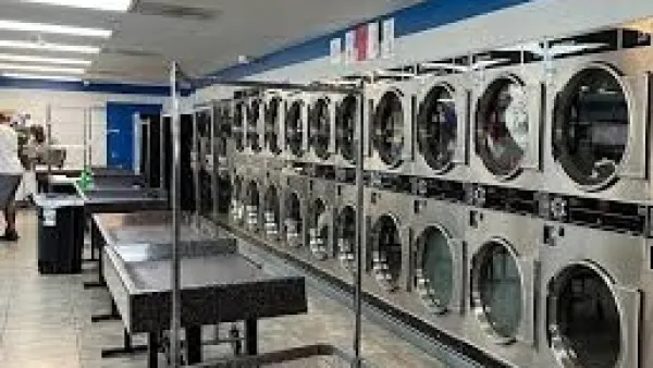 Interior of a laundromat with rows of washing machines and folding tables under bright fluorescent lights.