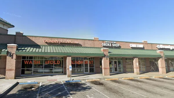 Strip mall with laundromat, smoke shop, and beauty salon under clear blue sky with green awnings.
