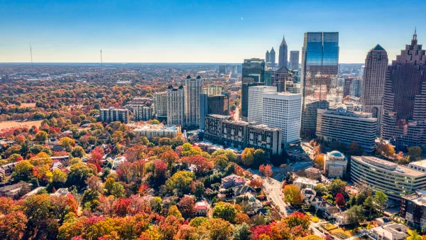 Aerial view of a city skyline with autumn trees showing vibrant red, orange, and green foliage under a clear blue sky.