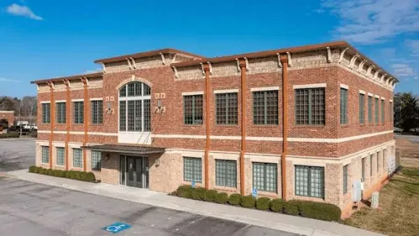 Two-story brick commercial building with large windows under a blue sky and handicapped parking spots in front.