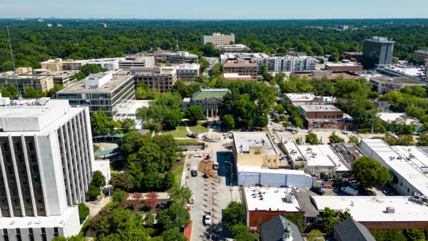 Aerial view of a cityscape with buildings, tree-lined streets, and construction work under a clear blue sky.