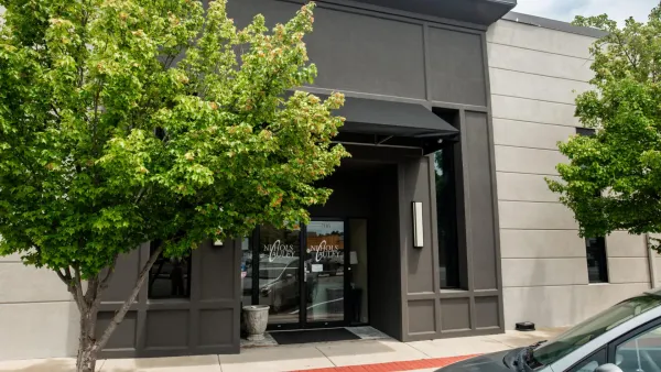 Stylish building entrance with dark framed glass doors, green trees, and a parked silver car outside.