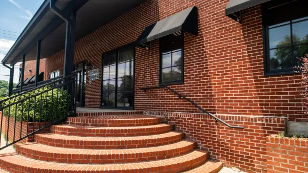 Curved brick steps leading to a black awning entrance on a red brick building with metal railings and plants.