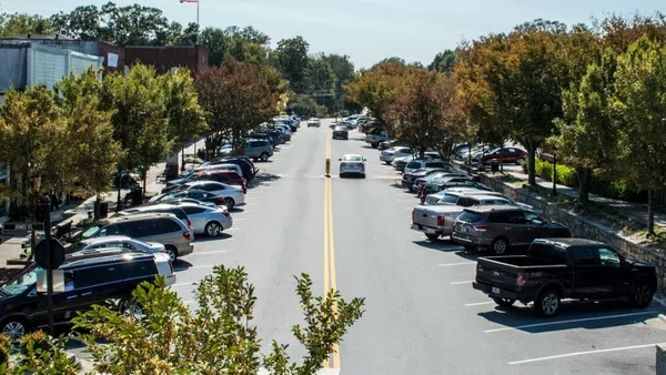 Small town main street lined with parked cars, trees, historic buildings, and flags on a sunny day