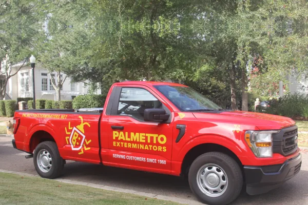 Red Palmetto Exterminators truck parked on a street with trees and buildings in the background.