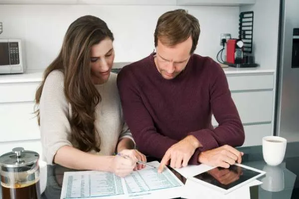 a man and a woman sitting at a counter with a spreadsheet and tablet