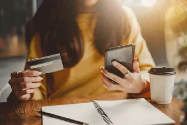 woman in café making purchase with credit card on cell phone