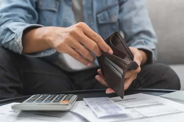 Person holding an empty brown wallet over bills and a calculator, suggesting financial stress or budgeting.
