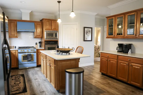 Spacious kitchen with wooden cabinets, blue stove, white countertops, kitchen island, and hanging lights over island.