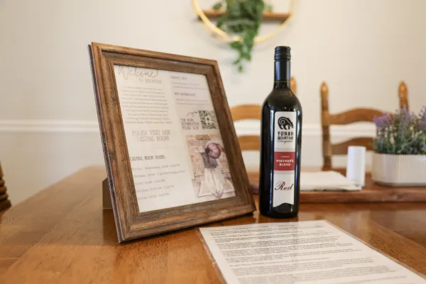 Bottle of Yonah Mountain Vintners Blend red wine next to a framed tasting room information sign on a wooden table.
