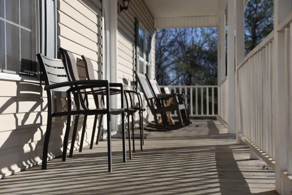 Sunlit porch with black chairs and rocking chairs casting shadows on wooden floor in daytime