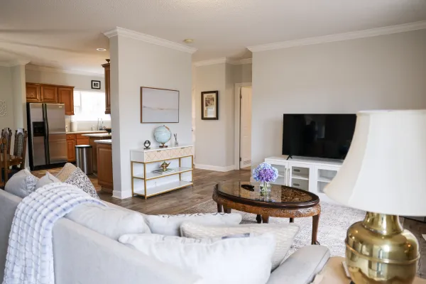 Bright modern living room with gray sofa, wooden coffee table, flat-screen TV, and open kitchen in background.