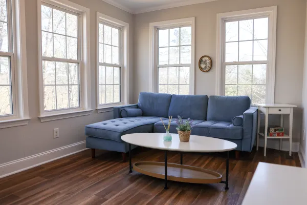 Cozy living room with a blue sectional sofa, white oval coffee table, hardwood floors, and large windows letting in natural light