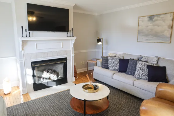 Modern living room with gray sofa, patterned pillows, fireplace, wall-mounted TV, and round coffee table with decor.