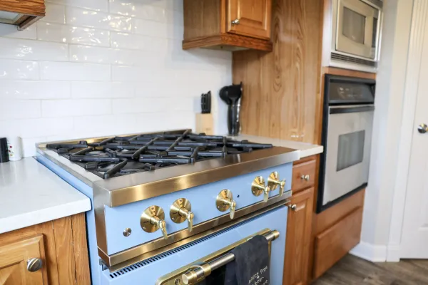 Modern kitchen with a stainless steel gas stove featuring four burners and gold knobs, surrounded by wooden cabinets.