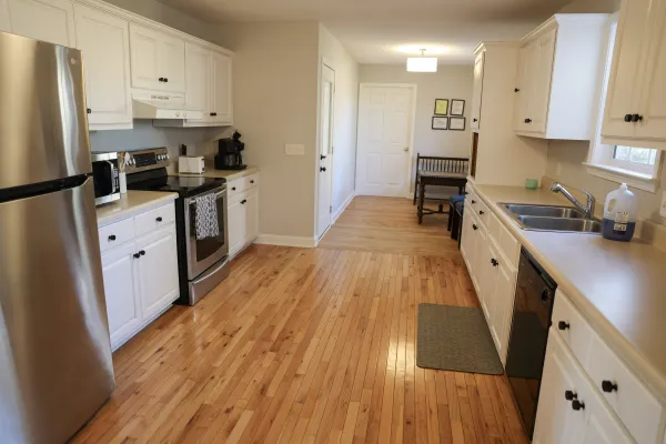 Modern kitchen with white cabinets, stainless steel appliances, hardwood floors, and beige countertops under bright lighting