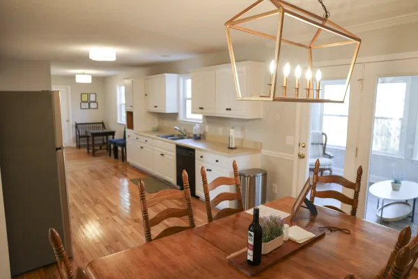 Bright kitchen with white cabinets, wooden dining table, pendant light, and hardwood floors in an open layout.