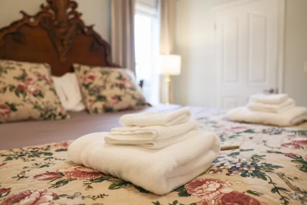 White folded towels placed on a floral bedspread in a cozy bedroom with wooden headboard and soft lighting.