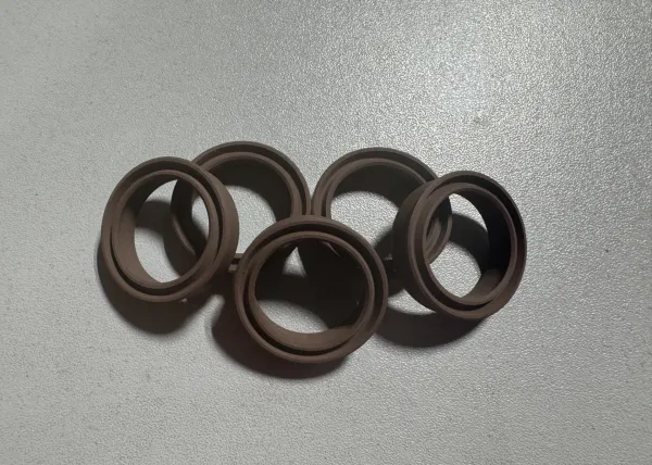 Stack of five dark brown rubber O-rings casting shadows on a textured gray surface