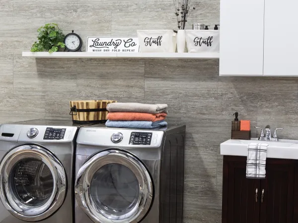 Modern laundry room with stainless steel washer and dryer, folded towels, and organized shelves with decor.