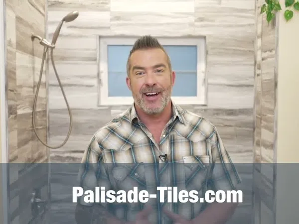 Man in plaid shirt presenting in a modern bathroom with tiled walls and a showerhead.