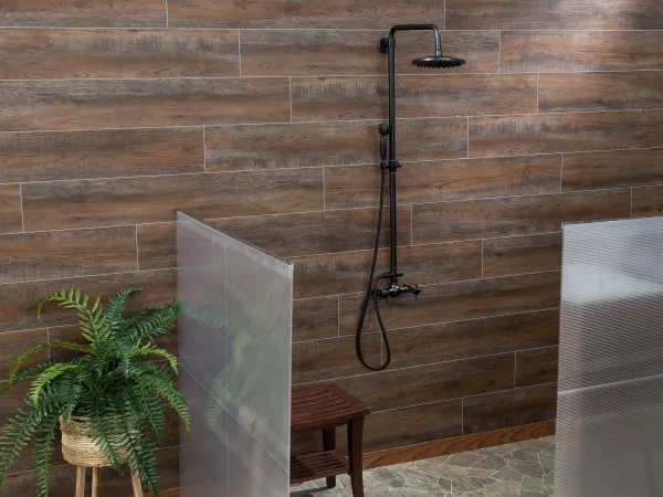 Modern shower area with black rain shower fixture, wood-look tile wall, small wooden bench, and green potted plant.