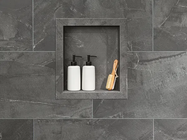 Two white pump bottles and a wooden brush placed in a recessed niche within dark gray stone tiles in a bathroom.