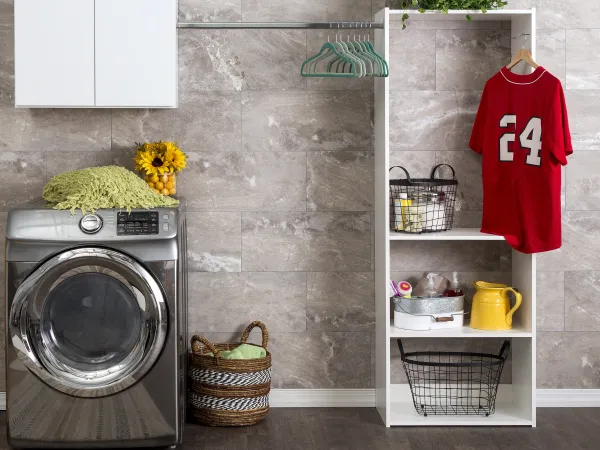Modern laundry room with front-load washer, open shelving, hanging red jersey, and decorative baskets and plants.
