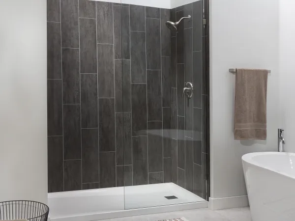 Modern bathroom with glass shower enclosure, dark tiled walls, freestanding tub, and neutral accessories.