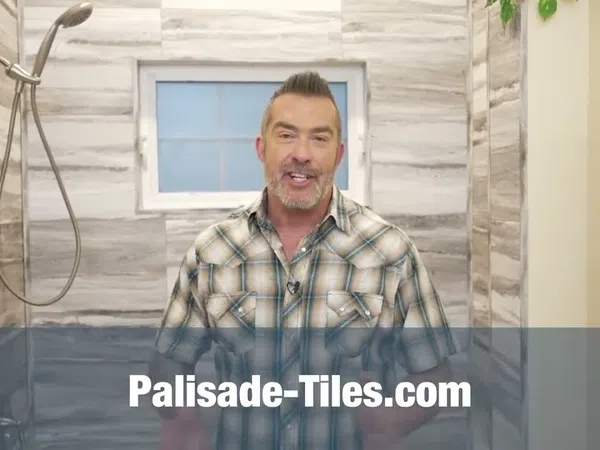 Man in a plaid shirt stands in a modern bathroom with tiled walls and a window behind him.