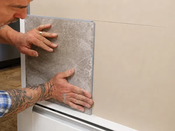 Man with tattoos installing large stone tile on wall indoors, focusing on precise placement and alignment.