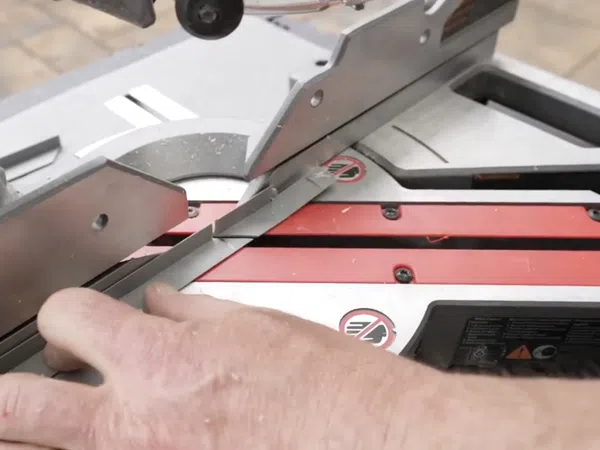 Close-up of a hand guiding trim piece through a red and gray miter saw cutting at an angle.