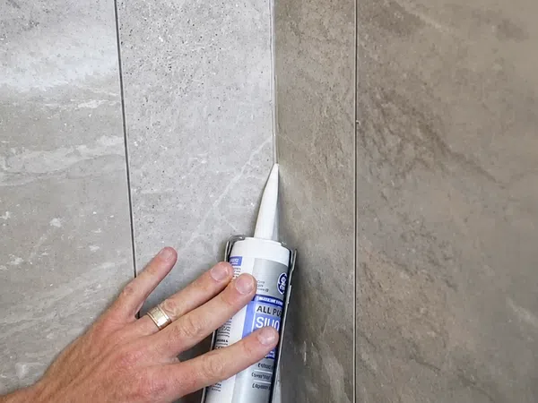 Person applying silicone sealant to a tiled corner joint for waterproofing and finishing.