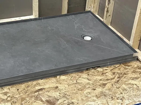 Black stone shower base installed in wooden frame with drain hole ready for tiling and plumbing.