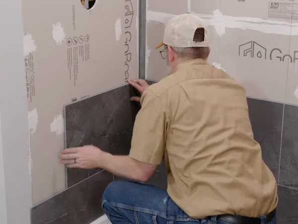 Man installing dark stone tiles on a bathroom wall over waterproof GoBoard cement board backing.