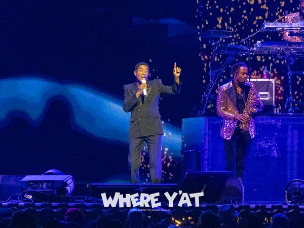 Singer performing on stage with saxophonist and DJ, vibrant lighting and audience visible in foreground